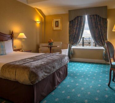 Elegant hotel room with cosy double bed, plush carpet, and a window view, offering comfort and peaceful relaxation.