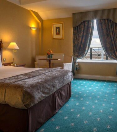 Elegant hotel room with cosy double bed, plush carpet, and a window view, offering comfort and peaceful relaxation.