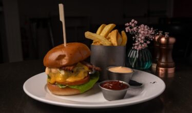 Gourmet beef burger with fries and sauces on elegant white plate, creating a delicious dining experience at the hotel restaurant.