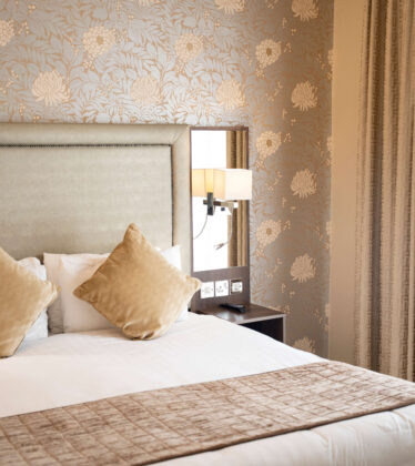 Elegant hotel room with plush bedding, floral wallpaper, soft lighting, and modern amenities for a relaxing stay.