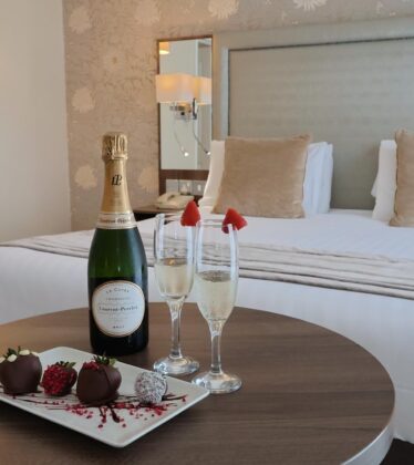 Luxurious hotel room with king-sized bed, champagne, and chocolate-covered strawberries, ideal for romantic getaways.