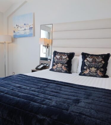 Elegant hotel room with plush bedding, chic decor, spacious seating, cosy lighting, and scenic artwork.