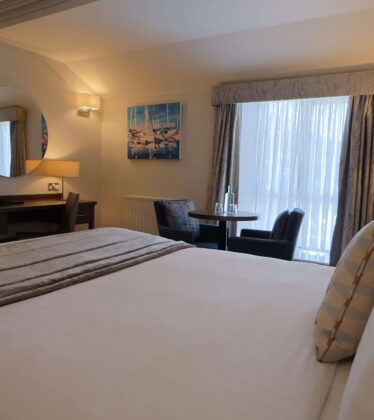 Spacious hotel room with a plush king-size bed, cosy seating area, modern decor, and large window for natural light.