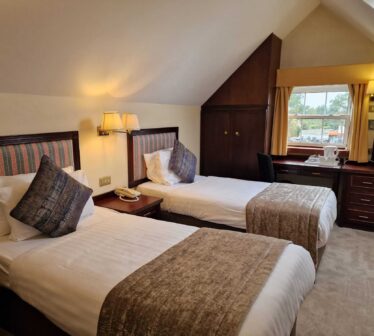 Cosy hotel room with twin beds, plush cushions, warm lighting, and a scenic view; ideal for a relaxing getaway.
