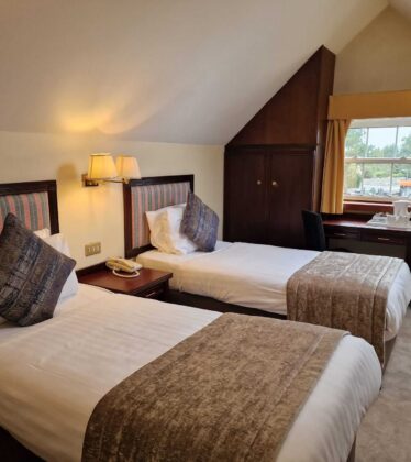 Cosy hotel room with twin beds, plush cushions, warm lighting, and a scenic view; ideal for a relaxing getaway.