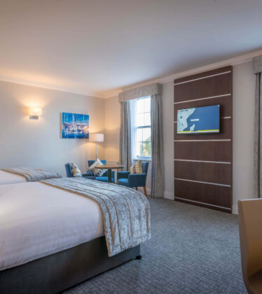 Spacious hotel room with twin beds, elegant decor, flat-screen TV, and views from large windows. Perfect for a relaxing stay.